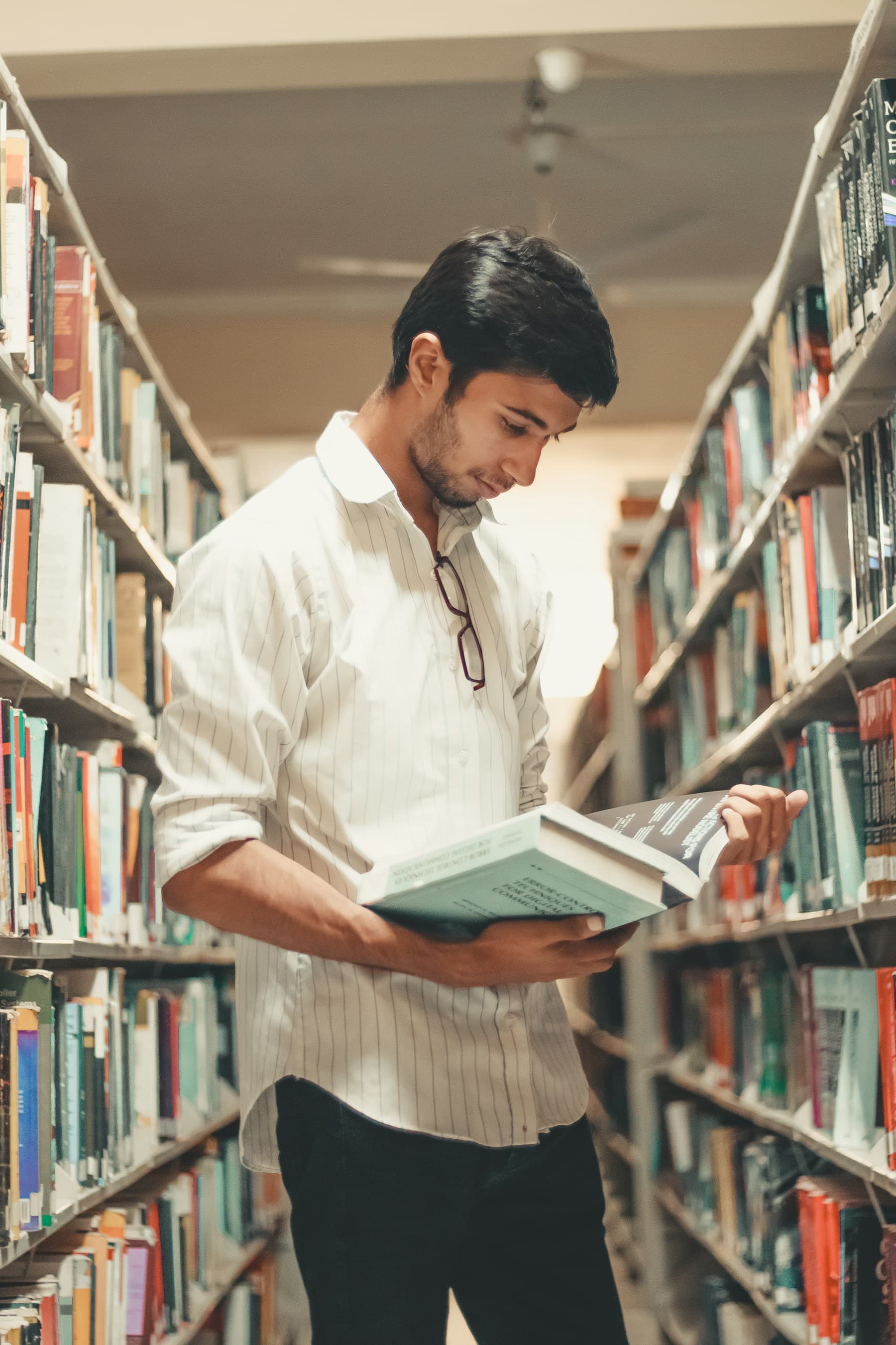A student reading in library stacks — the quiet work behind the numbers.