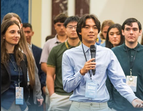 Tristan Tjetjep holding the microphone as a student speaker at the Day of AI festival, surrounded by fellow students.