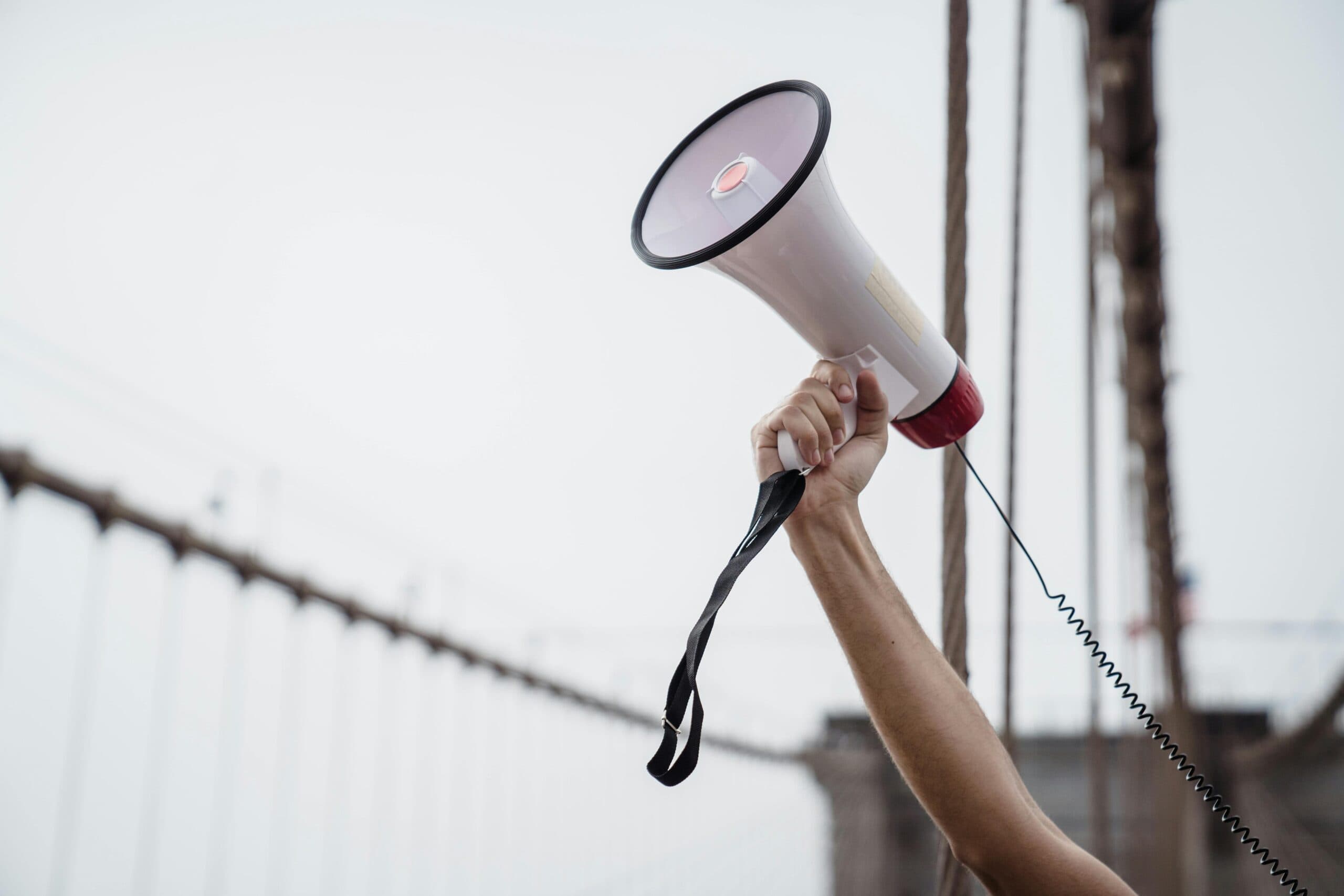 A hand raising a megaphone at an outdoor rally.